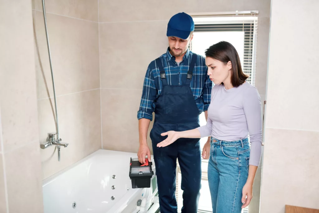 Young woman complaining to tile installation contractors about drain in bathtub or pipe and showing him where the problem is